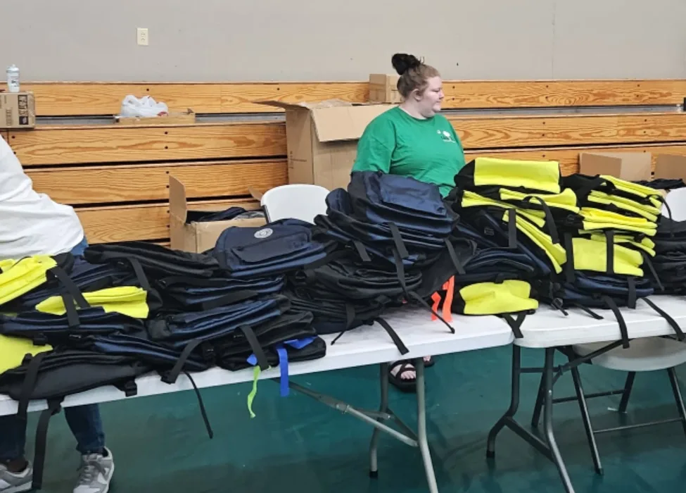 A volunteer behind long tables stacked with packed book bags before the give-away