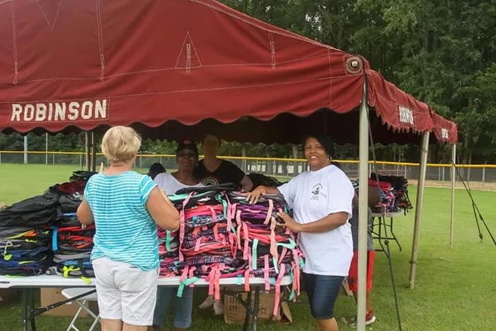 Volunteers laying out rows of book bags under a tent at the give-away