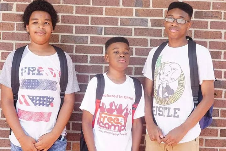 Three students standing against a brick wall wearing their new C.A.N. book bags