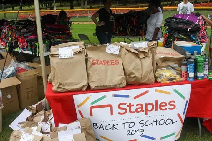 Packed supply bags lined up on a table beneath a Staples Back to School banner